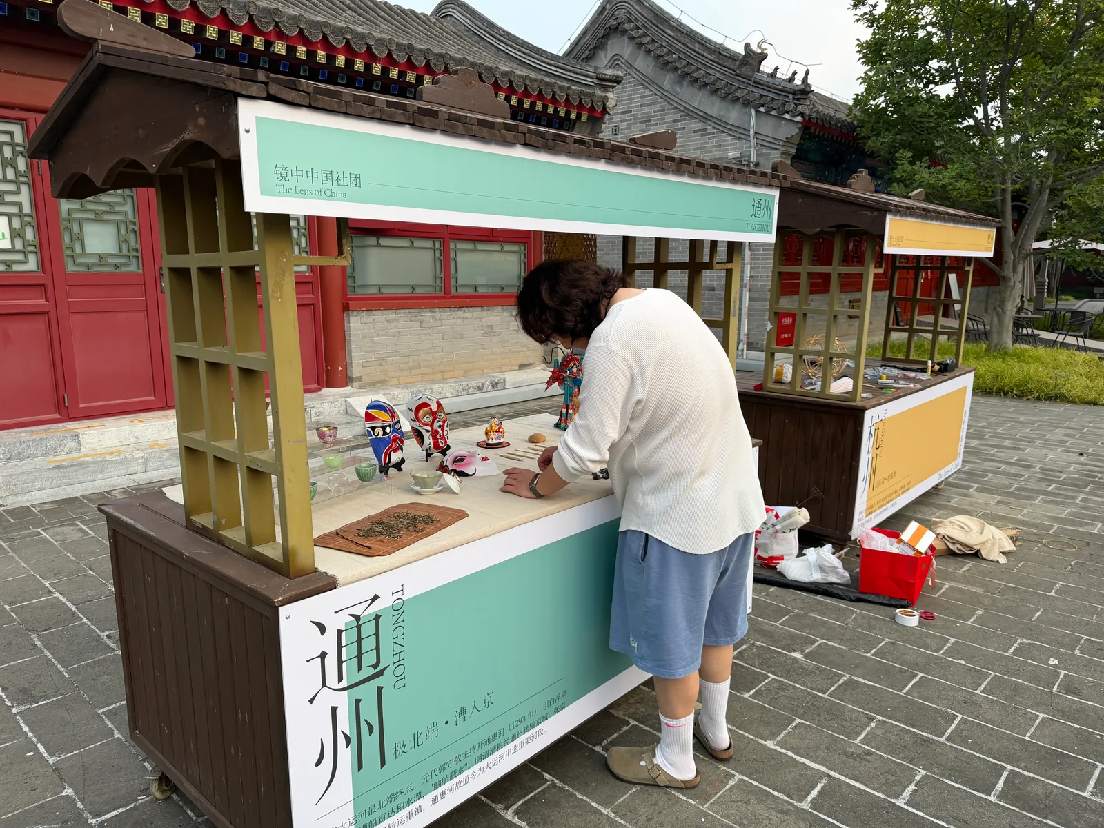A student setting up a display in a traditional red-walled courtyard.