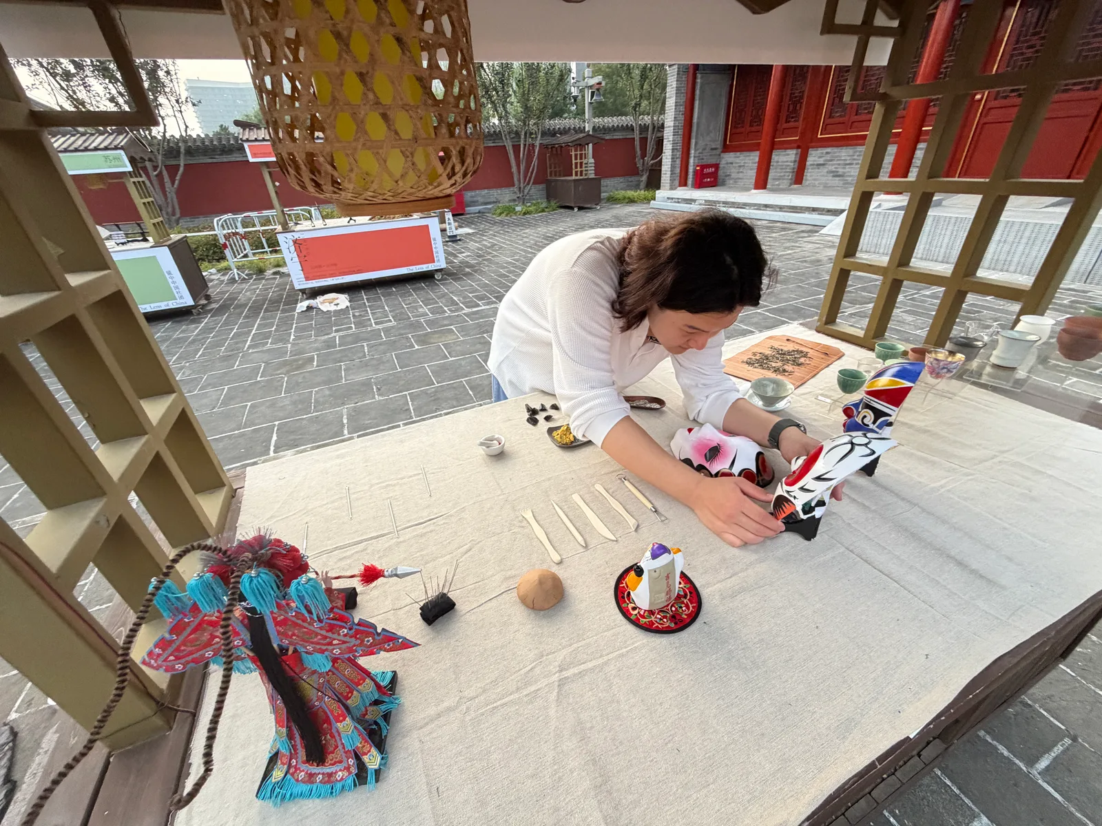 A student arranging opera masks and small craft objects at the Tongzhou exhibition display.